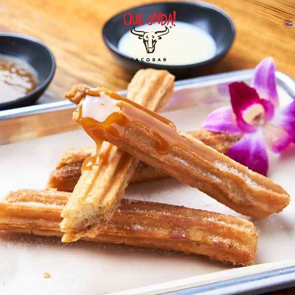 Que Onda Tacobar churros drizzled with caramel sauce, with dipping sauces and an orchid.