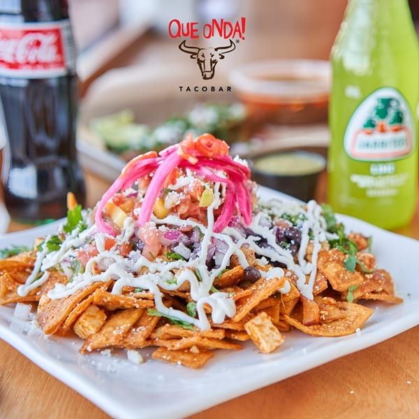 Que Onda Tacobar nachos with pickled onions, crema, and salsa, alongside a Coca-Cola and Jarritos.