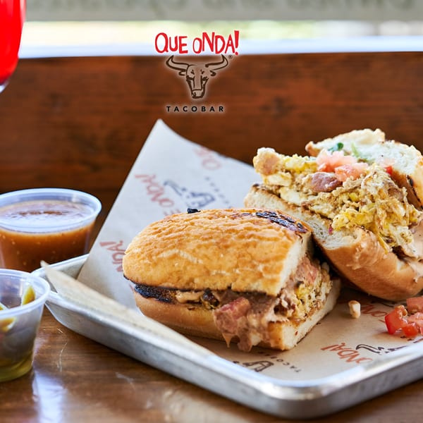 Two Que Onda Tacobar tortas with various fillings, salsa, and pickled onions on a metal tray.